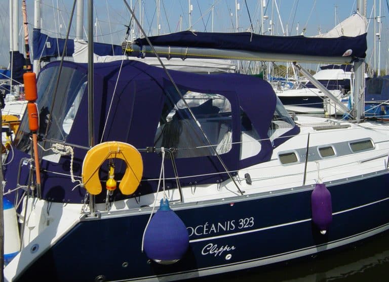 Cockpit enclosure for Beneteau Oceanis 323 with Tecsew Sprayhood Recover Type 2, featuring Sunbrella fabric and clear windows.