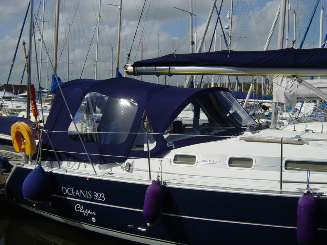 Cockpit enclosure for Beneteau Oceanis 323 with Tecsew Sprayhood Recover Type 2, featuring Sunbrella fabric and clear windows.