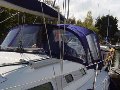 Cockpit enclosure for Beneteau Oceanis 323 with Tecsew Sprayhood Recover Type 2, featuring Sunbrella fabric and clear windows.